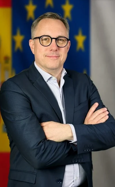 Consultor para pymes y empresas de brazos cruzados en traje frente a unas banderas