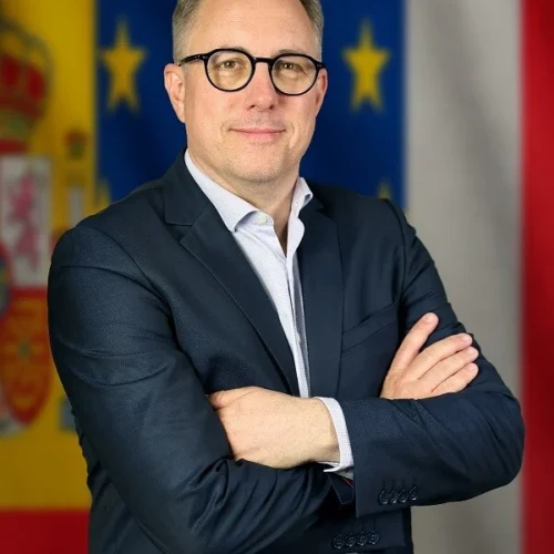 Consultor para pymes y empresas de brazos cruzados en traje frente a unas banderas